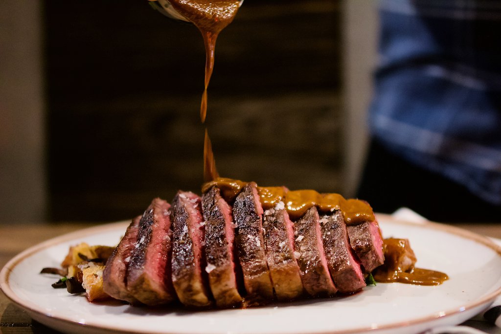 Photo of a sliced steak on a plate with sauce pouring on the top.